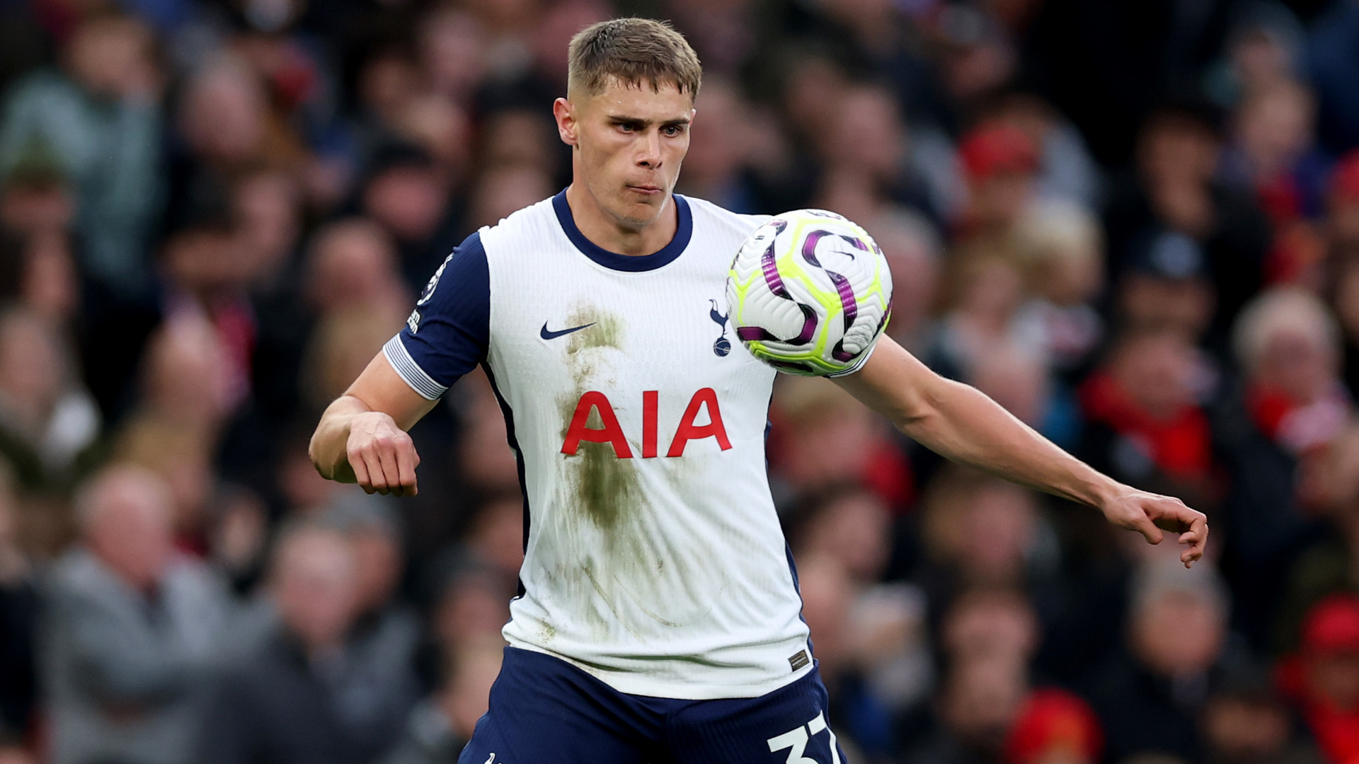 Micky van de Ven controls the ball in his white and navy blue Tottenham home shirt.