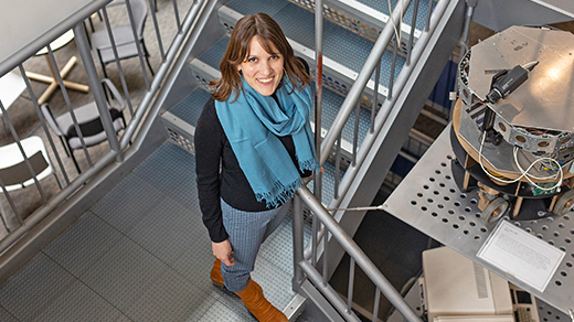 Ellie Pavlick in a blue scarf stands on a stairwell next to a shiny machine