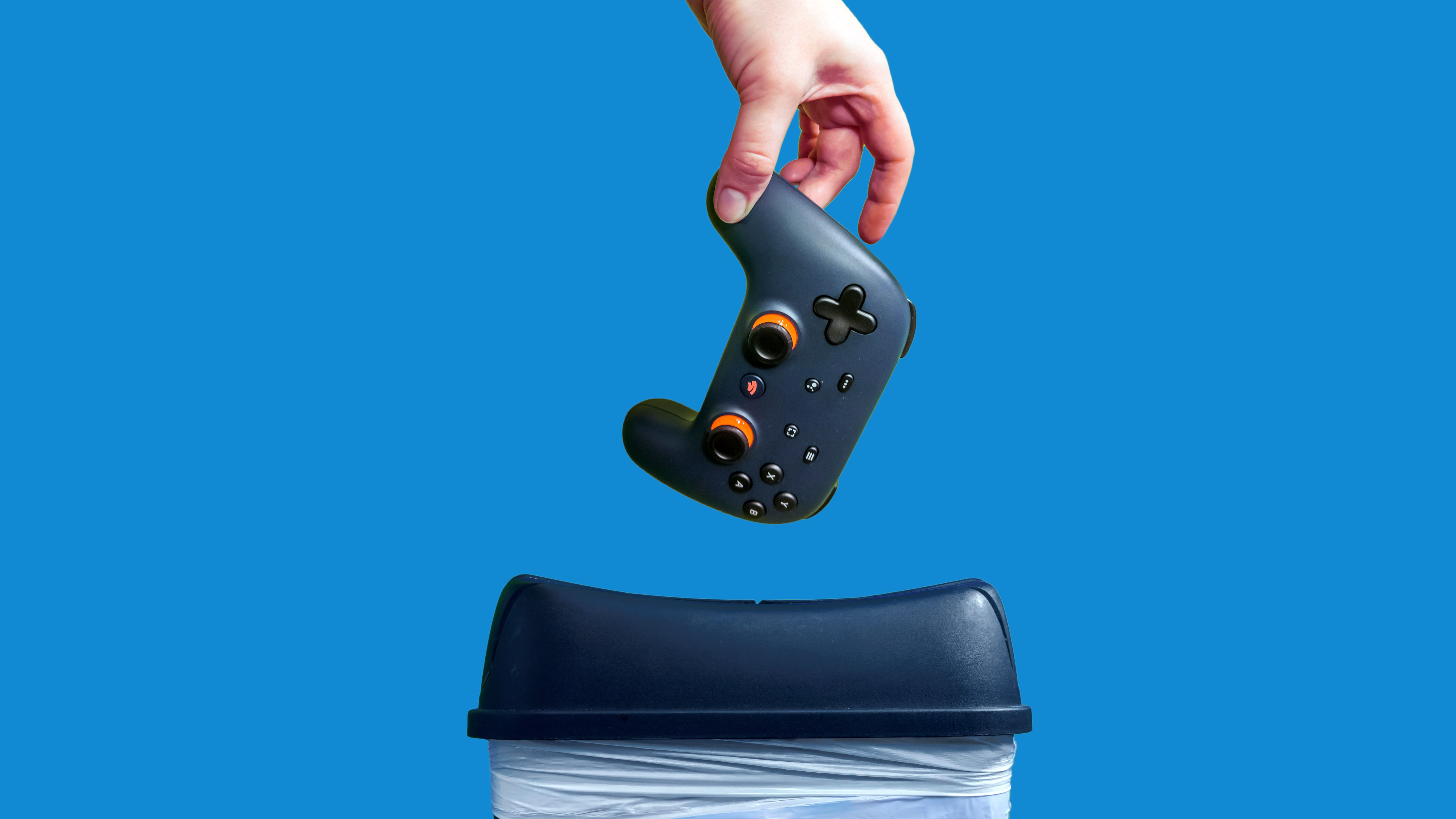 Closeup of a Google Stadia gaming controller being thrown into the trash can in frustration, against a colorful background