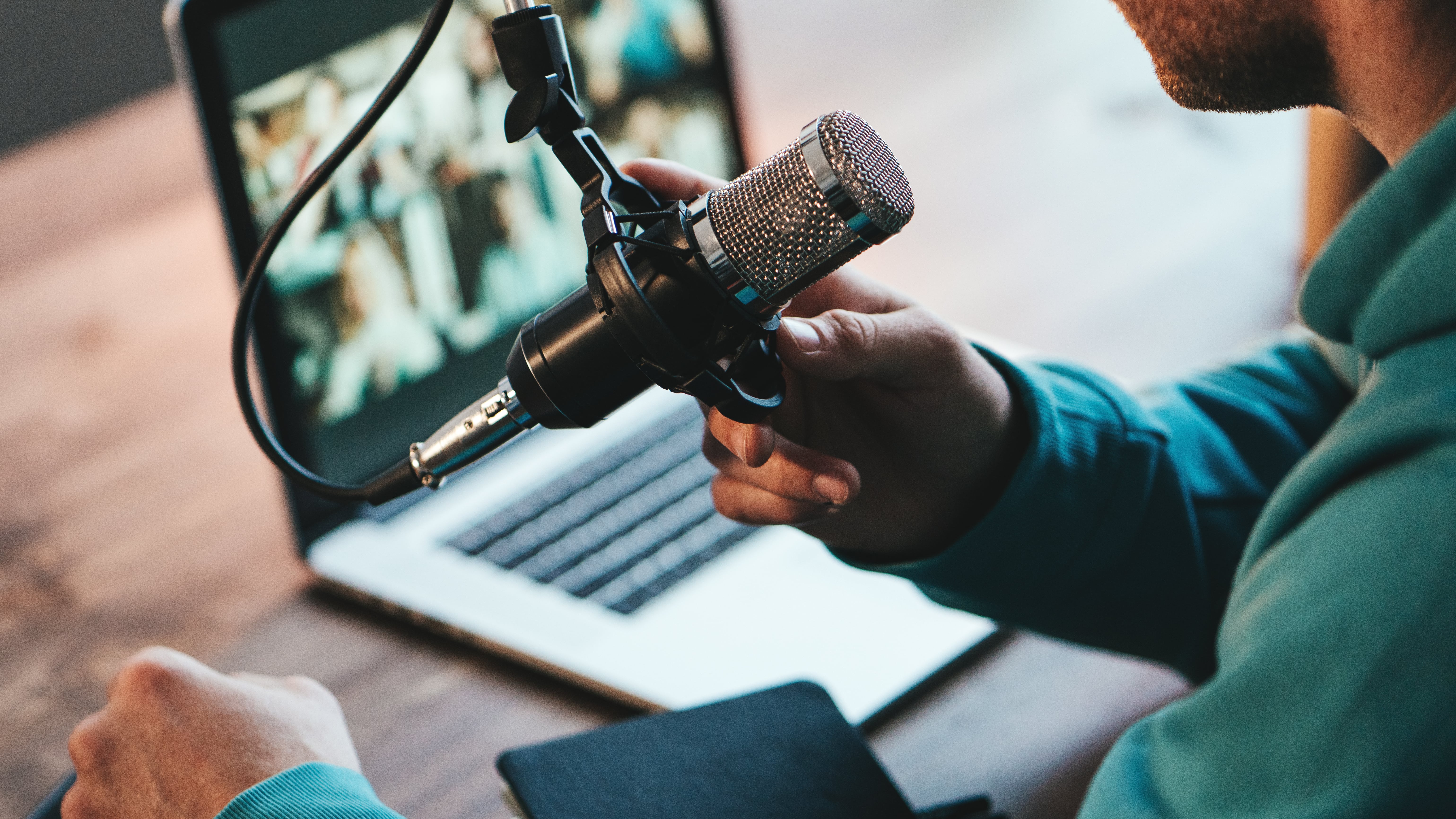 A man host streaming his audio podcast using microphone and laptop at his small broadcast studio, close-up