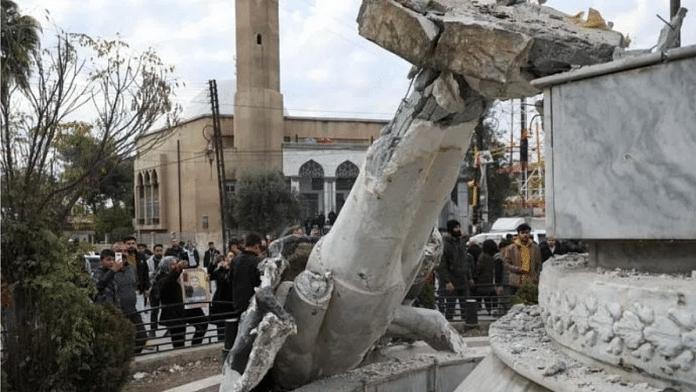 People stand near a damaged statue of former Syrian president Hafez al-Assad after Syrian rebels announced that they have ousted President Bashar al-Assad, in Qamishli, Syria on 8 December 2024. | Orhan Qereman | Reuters