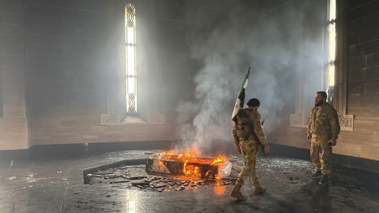 Rebel fighters stand next to the burning gravesite of Syria's late president Hafez al-Assad at his mausoleum in the family's ancestral village of Qardaha in the western Latakia province.(AFP)