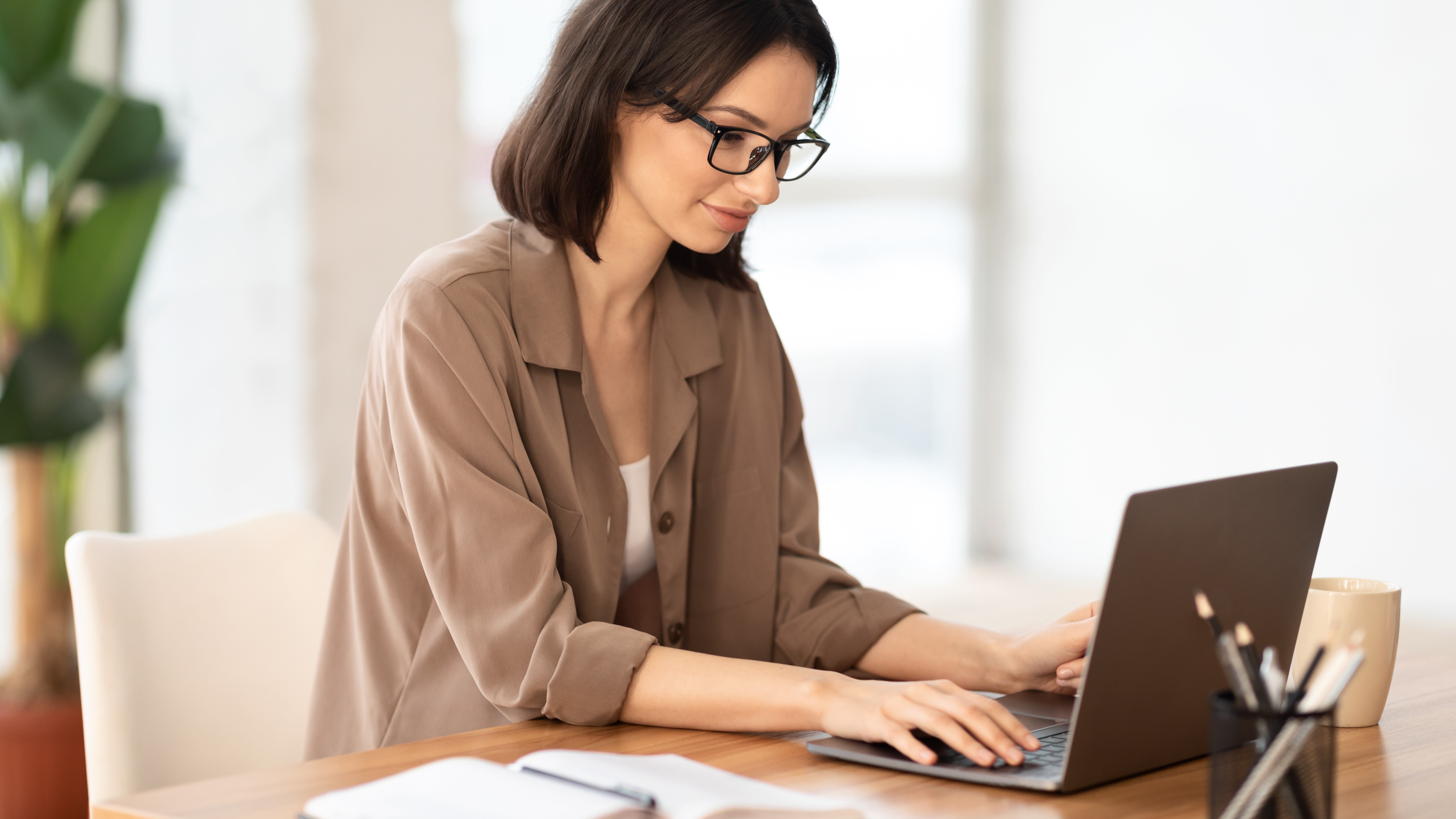 A woman sitting at a desk and using a laptop while sitting in a daylit room