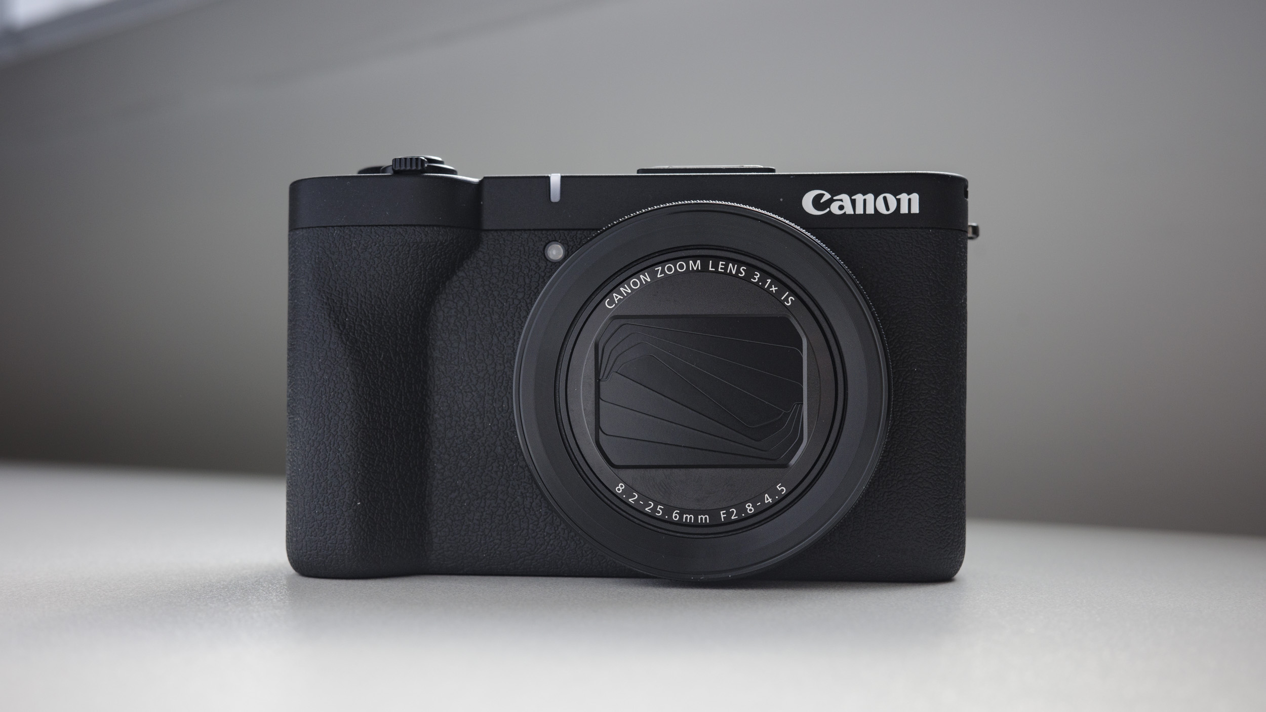 Canon PowerShot V1 compact vlogging camera on a white desk, lens folded away
