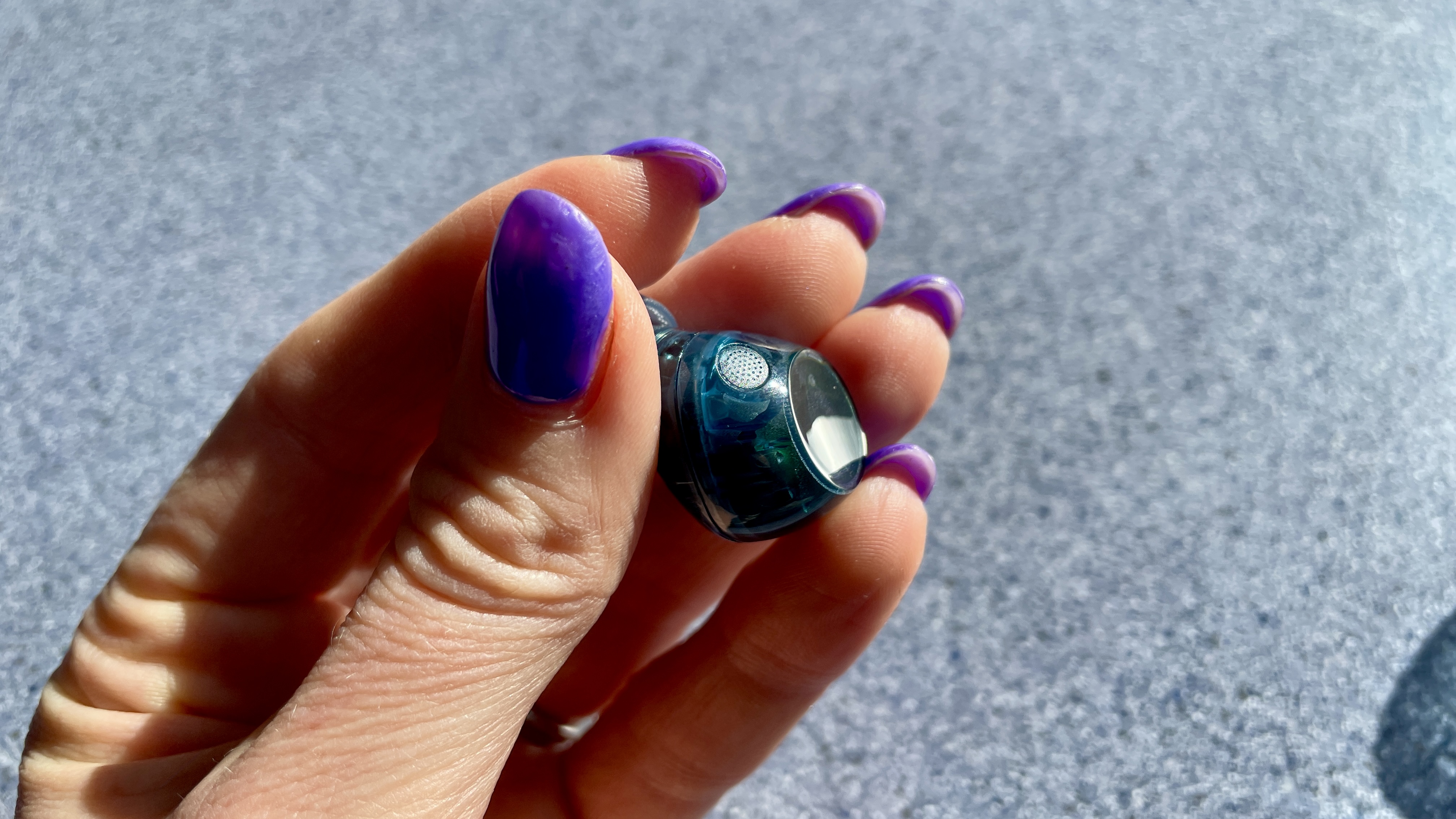 Sony WF-C710N earbuds in 'blue glass' on a grey table, with a woman's hand holding one of the earpieces