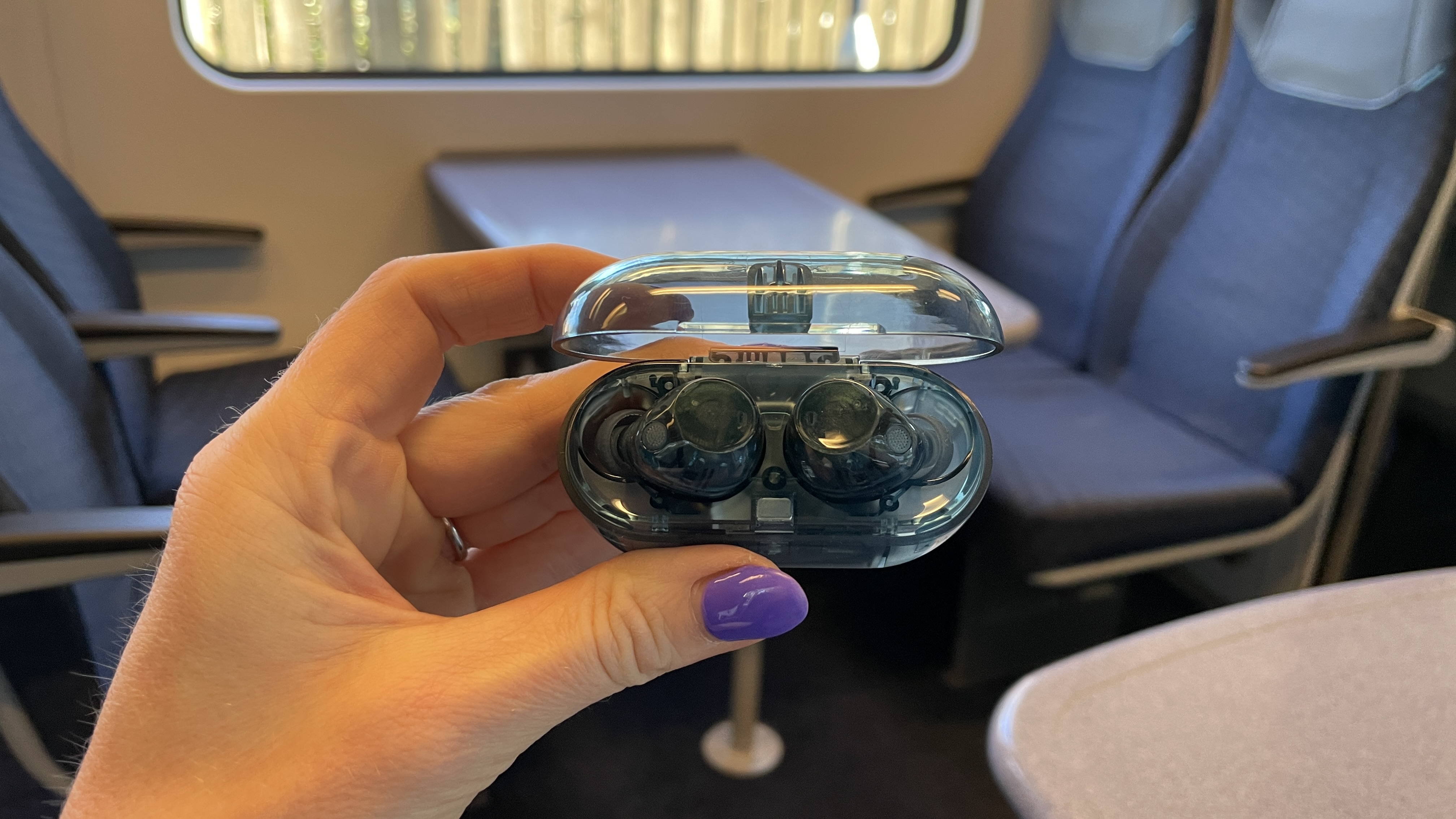 Sony WF-C710N earbuds in 'blue glass' on a grey table, with a woman's hand holding one of the earpieces