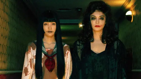 Two women with smudged makeup and blood stains stare at the camera