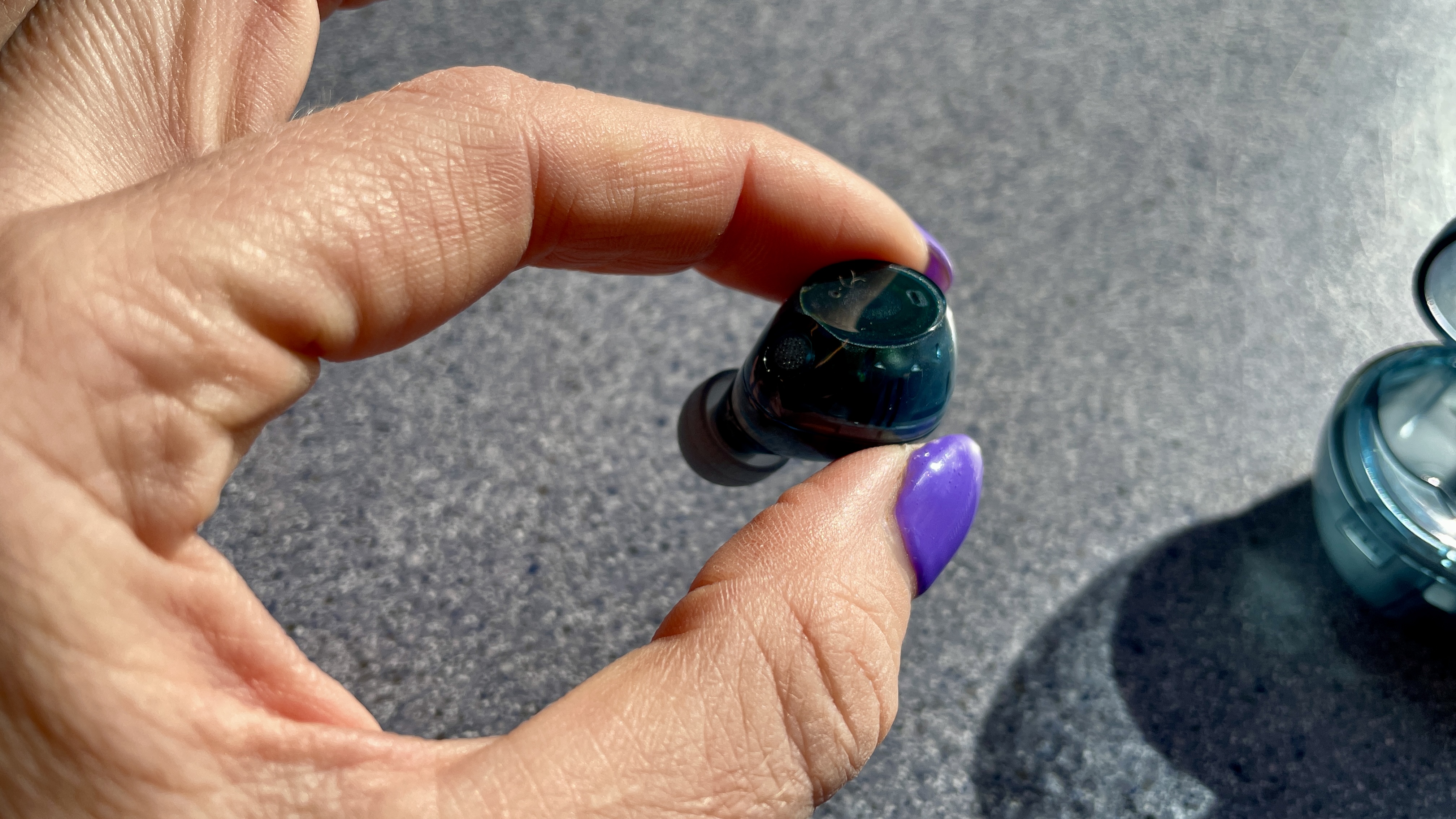 Sony WF-C710N earbuds in 'blue glass' on a grey table, with a woman's hand holding one of the earpieces